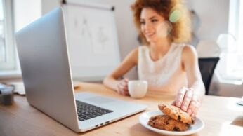 Smiling business woman drinking coffee with cookies on workplace